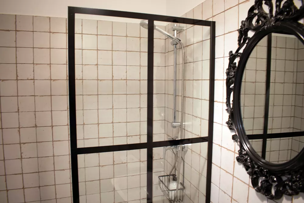Baño habitación con espejo y pie de ducha con mampara